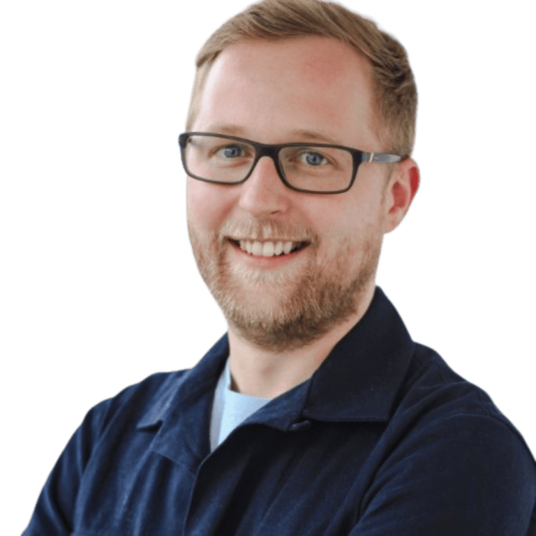 Smiling bearded man with glasses in a navy collared shirt, facing the camera against a plain background